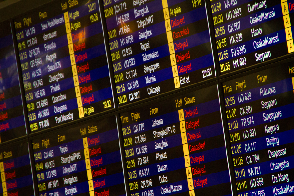 Close-up image of an airport departure board displaying various flight statuses, including delayed and canceled flights. The board shows columns for time, flight number, destination, hall, and status.